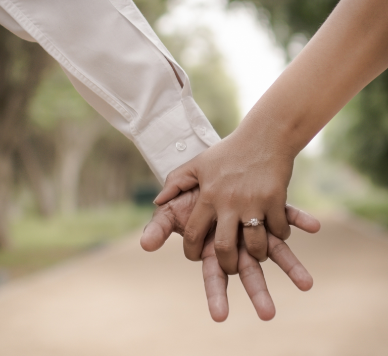 Zwei Hände, eine mit einem Ring, halten sich auf einem schmalen Weg.
