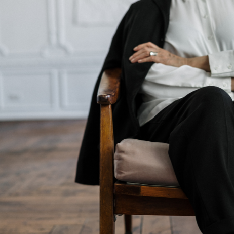 Eine Person sitzt entspannt auf einem Stuhl und trägt eine schwarze Jacke.